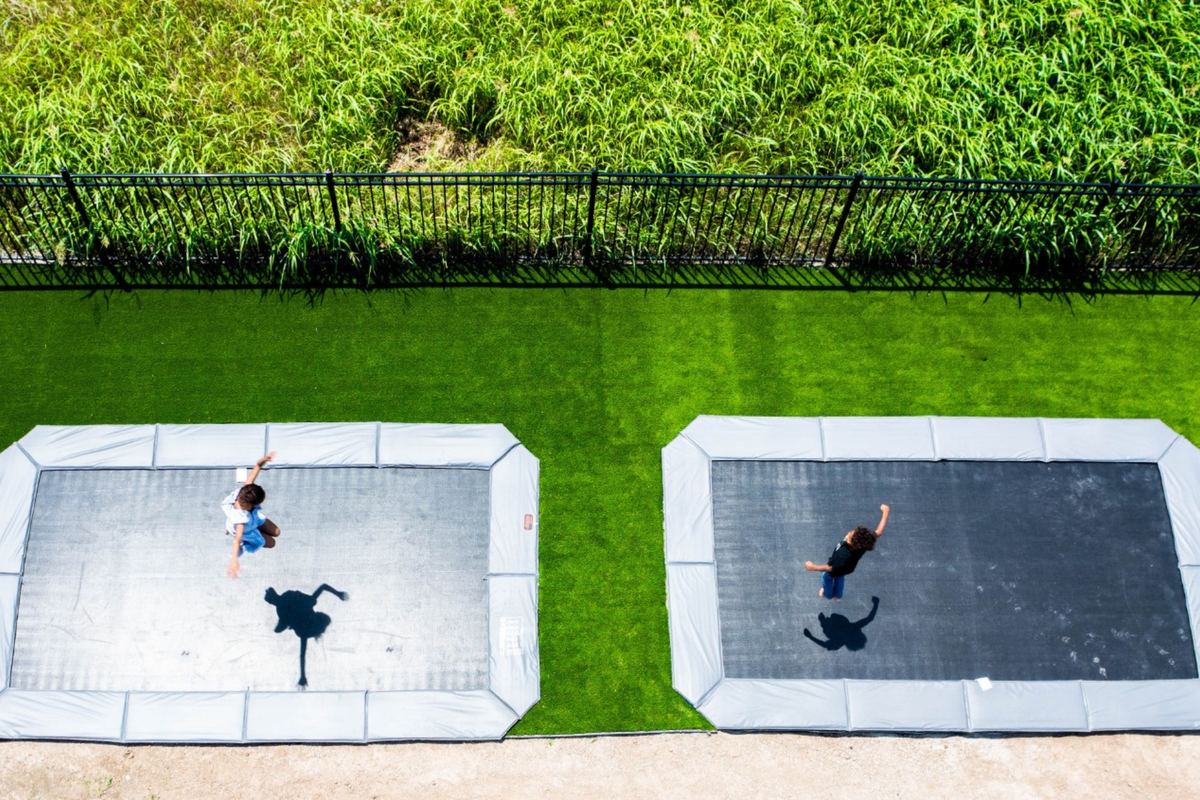 Two side-by-side in-ground trampolines with jumpers