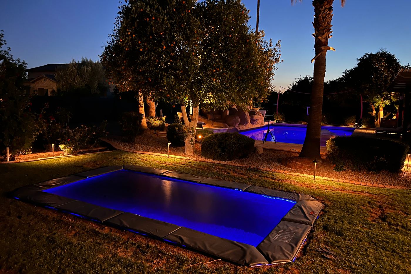 Rectangle in-ground trampoline with blue LED lights matching a lit pool at night