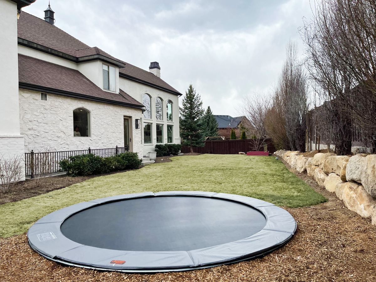 Round in-ground trampoline in a backyard with mountains behind it