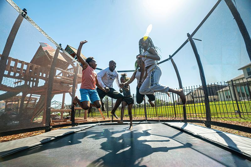 In-ground trampoline with a safety net enclosure and family jumping