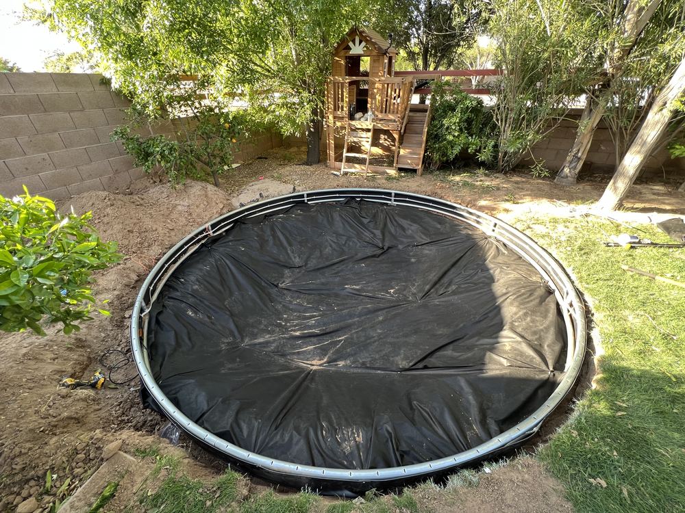 Weed barrier fabric being laid in a trampoline pit for drainage